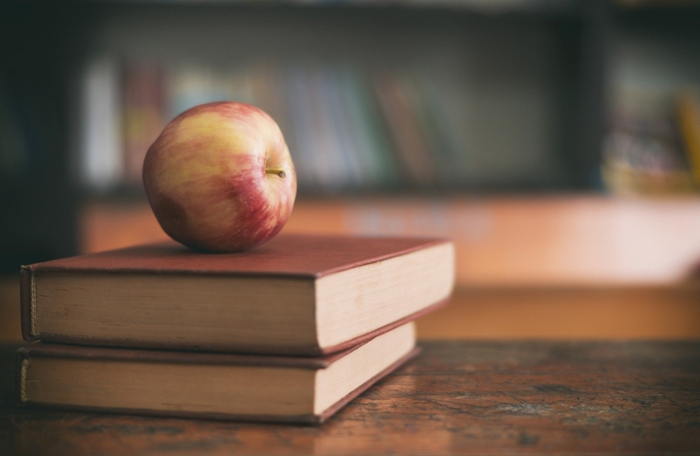 Apple sitting on a pile of books on a desk.