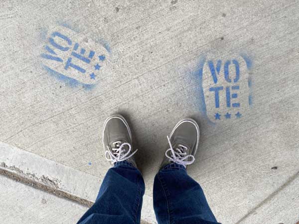Someone standing next to "vote" spray painted on sidewalk. 