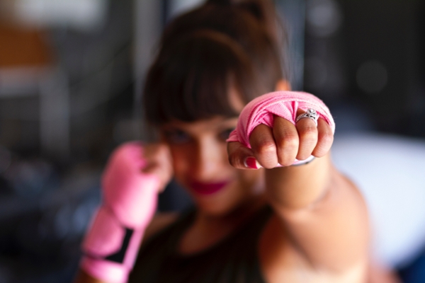 Women in a fighting stance with her fists wrapped in pink tape.