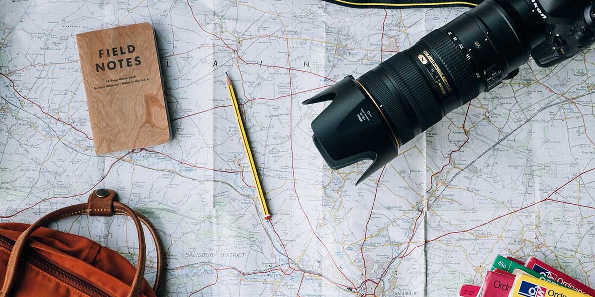 Flatlay of traveling essentials: map, pencil, bookbag, camera.