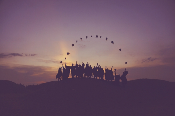 Silhouette of graduates standing on a hill tossing their gad caps.