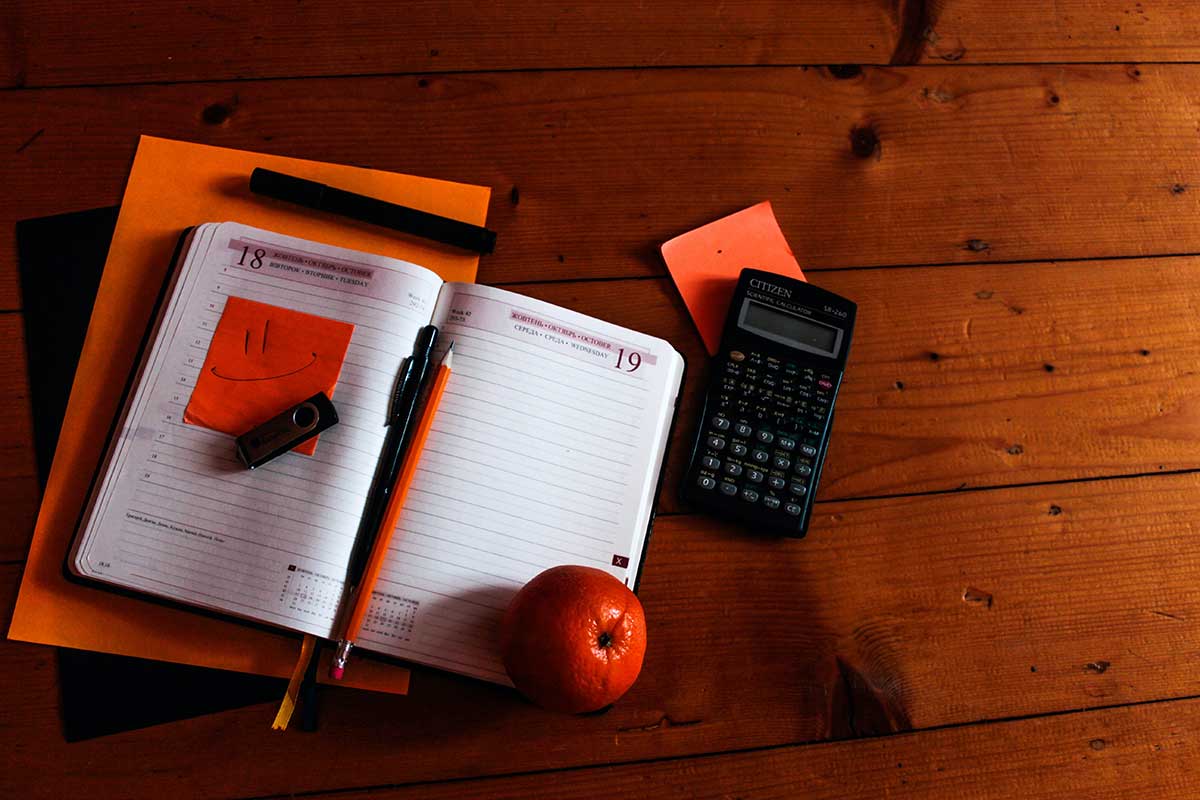 Notebook, calculator, and fruit sitting on a wooden desk.