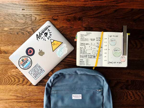 Flatlay of a desk covered with a laptop, bookbag, and notebook.