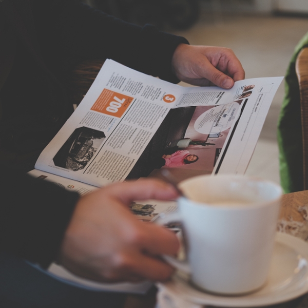 Person reading a newspaper while drinking coffee. 