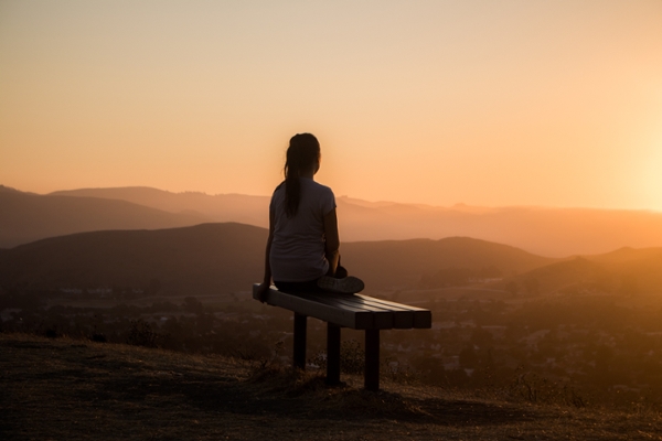 Woman sits on a bench overlooking a city.