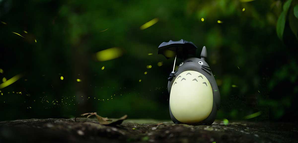 A small toy Totoro sits amongst greenery. 