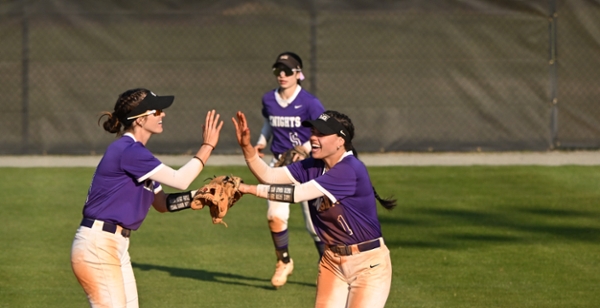 Knights softball players high five on the field during a game.