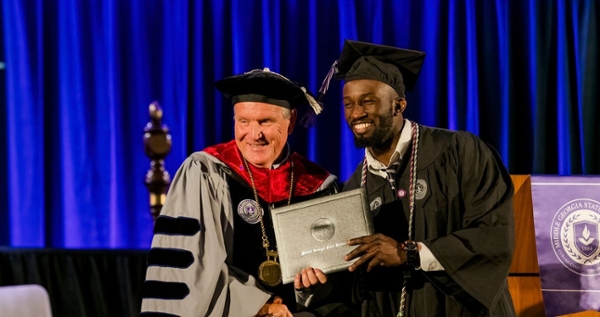 MGA President Chris Blake stands with a Black male graduate on stage as he hands him his diploma at spring 2025 commencement. 