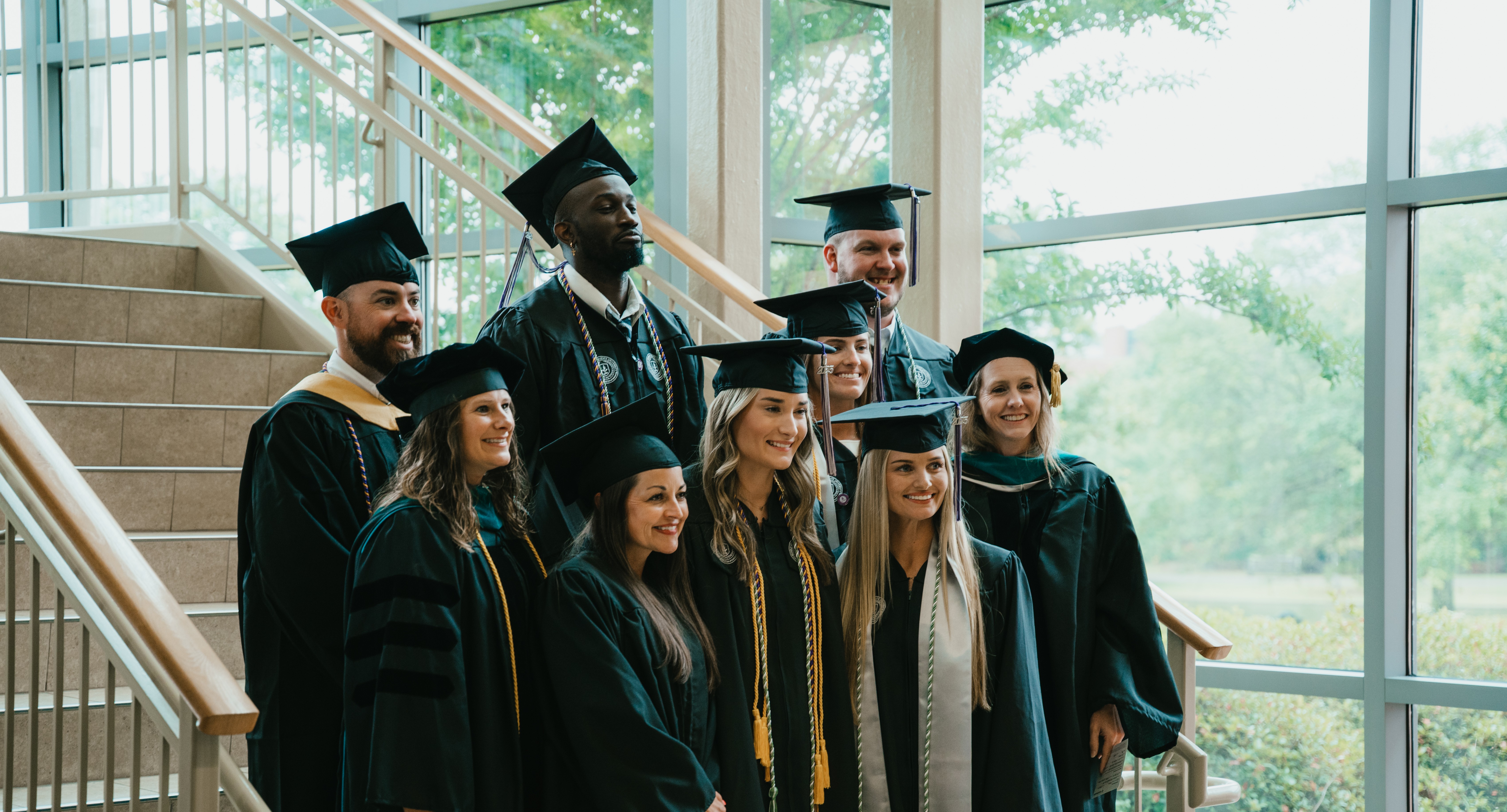 MGA graduates pose for a photo at spring 2025 graduation on the stairs of the recreation and wellness center on the Macon Campus.