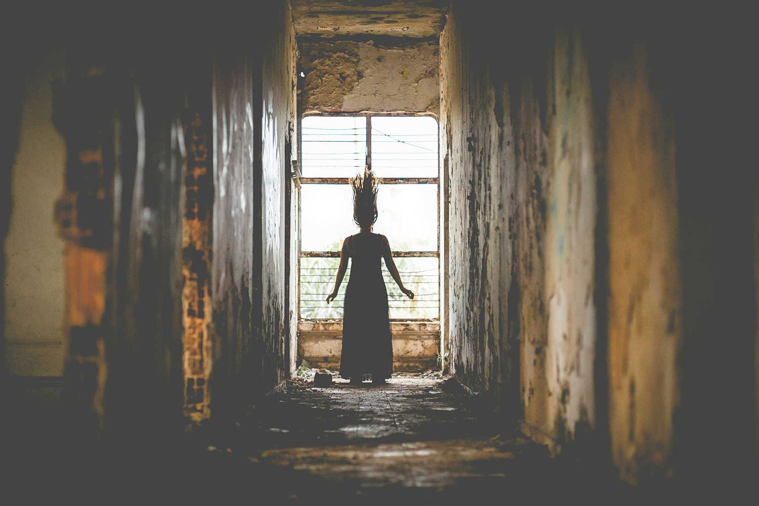 Scary silhouette of a woman stands at the end of a hallway. 