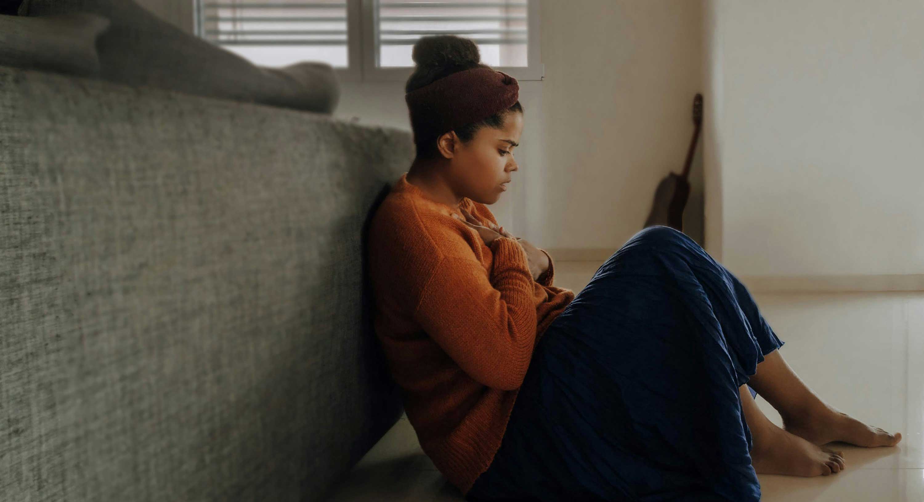 Woman sits on the floor holding her chest in pain. 