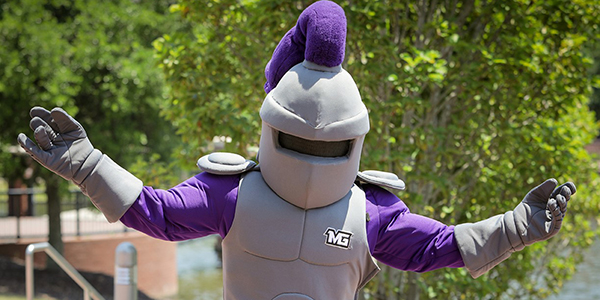 MGA mascot, Duke, walking outside in a victorious pose with his arms spread wide.