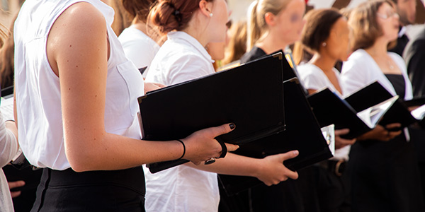 A side-profile view of a choir performing outdoors, dressed in black and white attire while holding open black music folders.