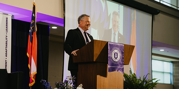 MGA Provost Dr. David Jenks smiles on stage from a podium at MGA’s 2025 Faculty & Staff Convocation.
