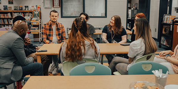 A group of students and faculty sitting around tables in a circle, engaged in conversation.