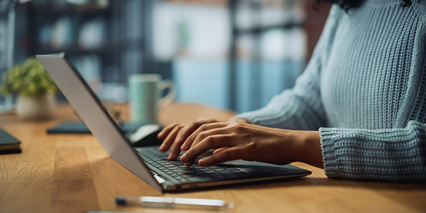 Image of a woman's hands typing at a laptop.