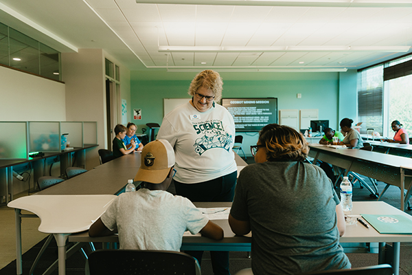 Camp facilitator assists participants with coding challenge