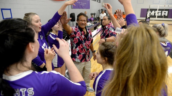 Coach Tui Tuionuu celebrating with the volleyball team in a huddle.