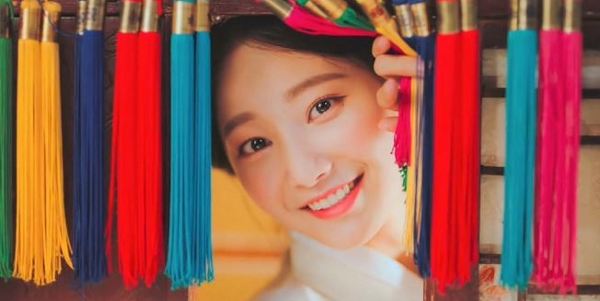 Korean woman smiling as she peeks through colored tassels. 