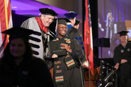 President Blake and a graduate pause for a photo during the graduation procession.