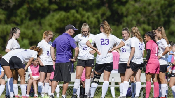 Coach Gill huddling with Knights women's soccer players during a game.