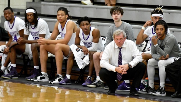 Coach Moe sitting on the bench with knights men's basketball players. 