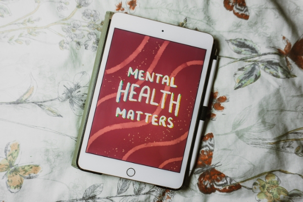 iPad laying on a bed displaying a graphic of abstract art that reads "mental health matters." 
