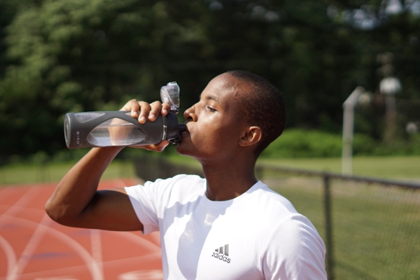 Man in athletic wear drinking water from a bottle on a track.