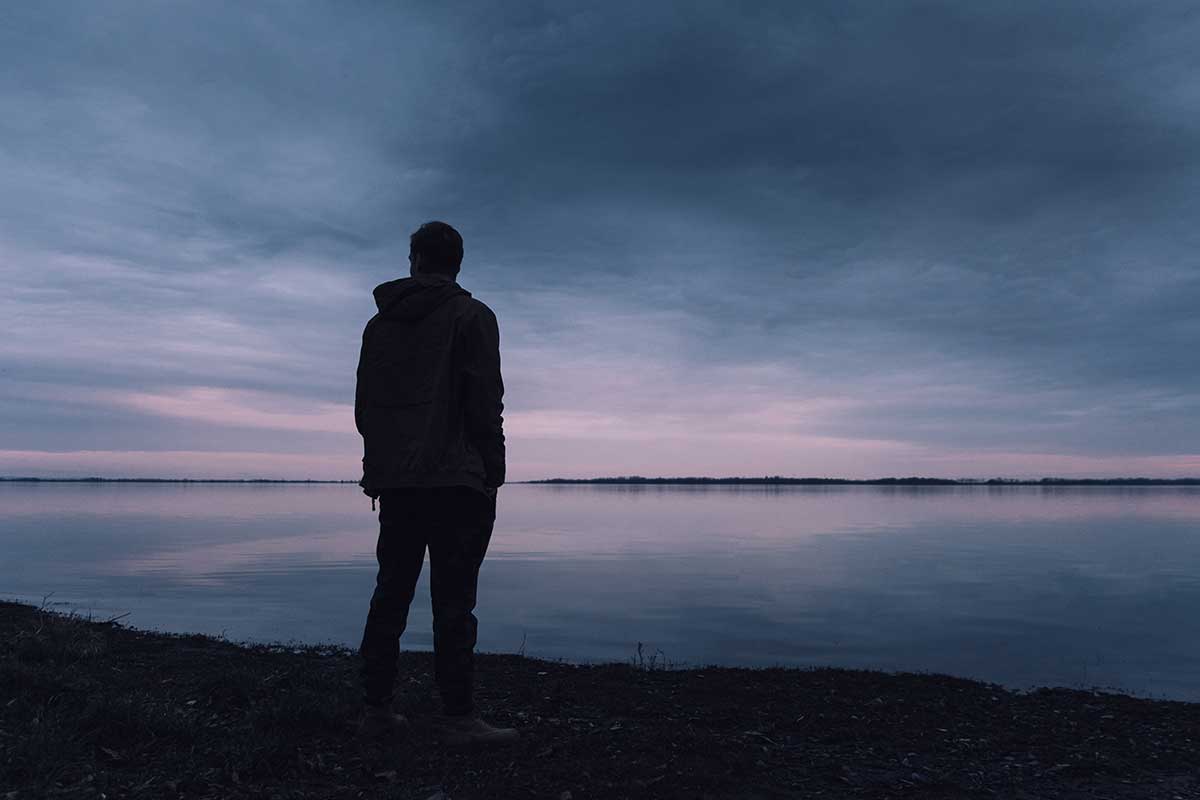 Silhouette of a man standing near a body of water. 