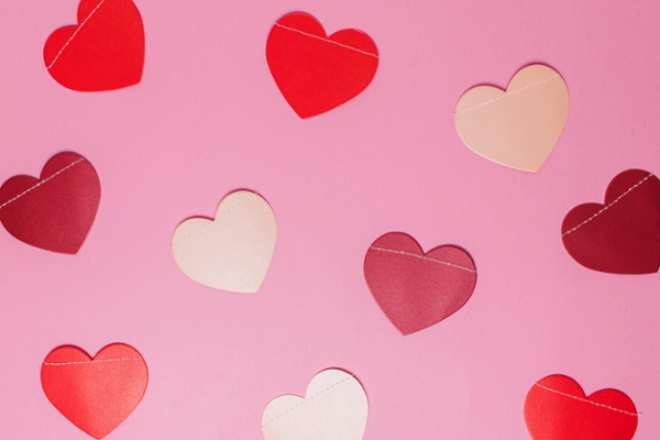 Flatlay of valentine paper hearts on a pink backdrop.