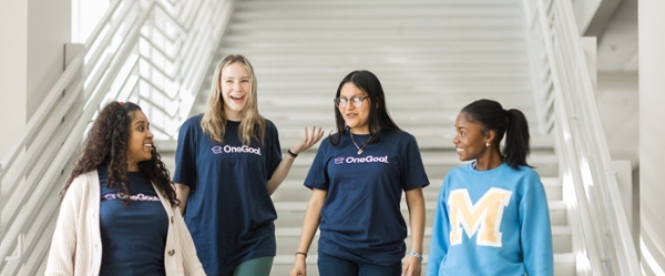 Students wearing OneGoal shirts walking and talking on campus.