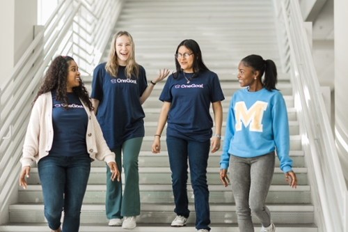 Students wearing OneGoal shirts walking and talking on campus.