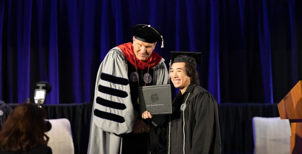 MGA President Chris Blake shakes hand with a male graduate as he crosses the stage at commencement. 