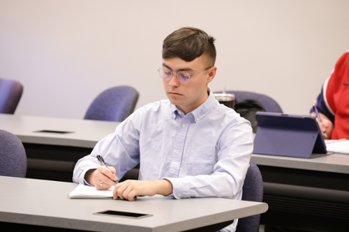 Male student takes notes during class. 