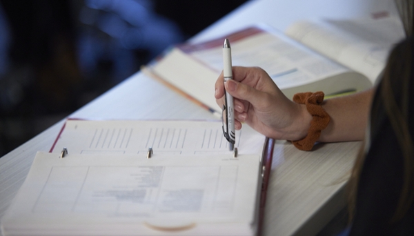 Close up photo of a student's hand taking notes and an open textbook. 