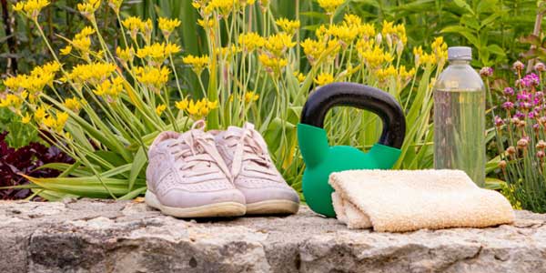 A pair of shoes, water bottle, weights, and a towel sitting on a rock in a garden.