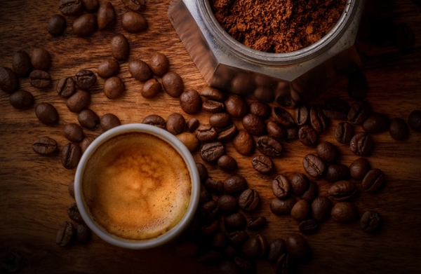 A latte and coffee beans, both whole and ground, sit on a wooden surface.