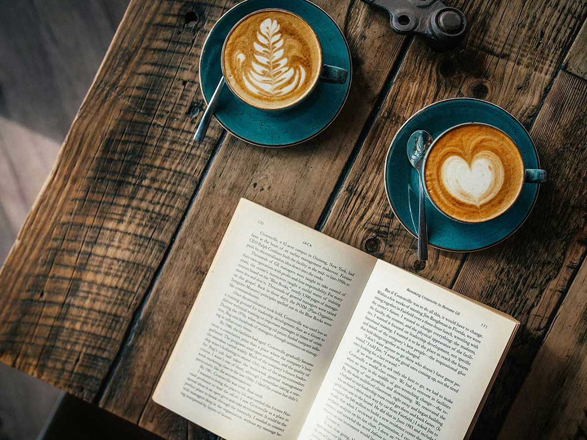 Open book laid on a table next to lattes. 