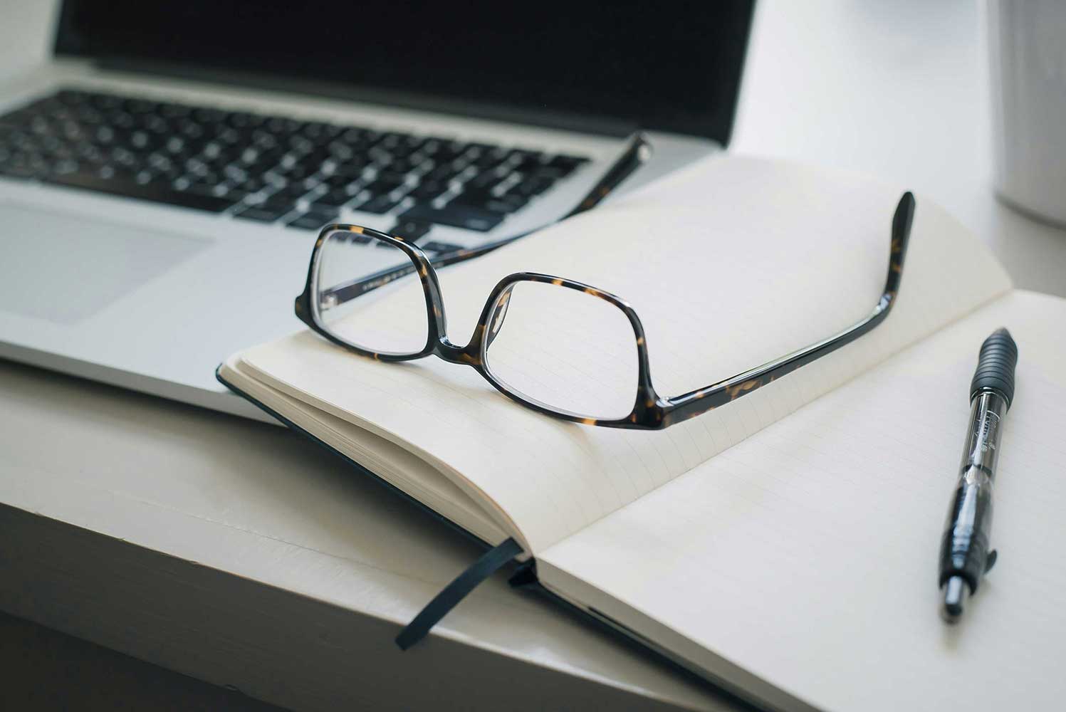 Glasses and pen rest on a blank journal. 