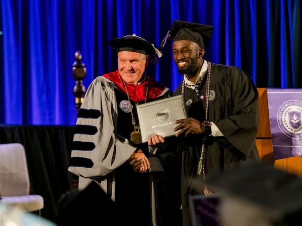 MGA President Chris Blake stands with a Black male graduate on stage as he hands him his diploma at spring 2025 commencement. 