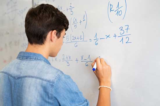 Male student solves math equations on a white board. 