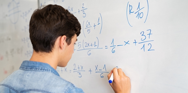 Male student solves math equations on a white board. 