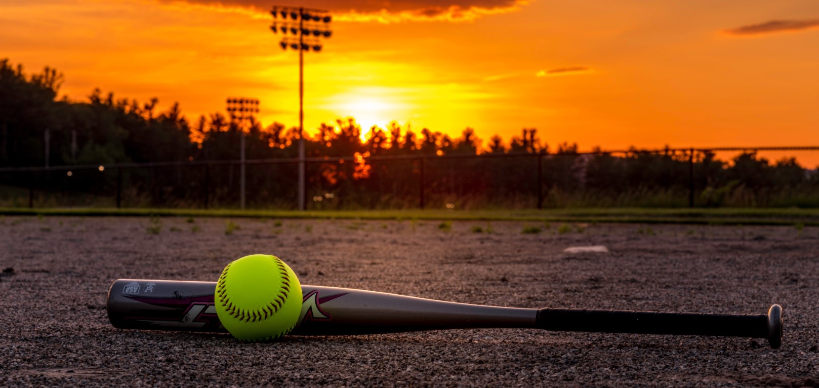 Bat and softball sit on cement at sunset.