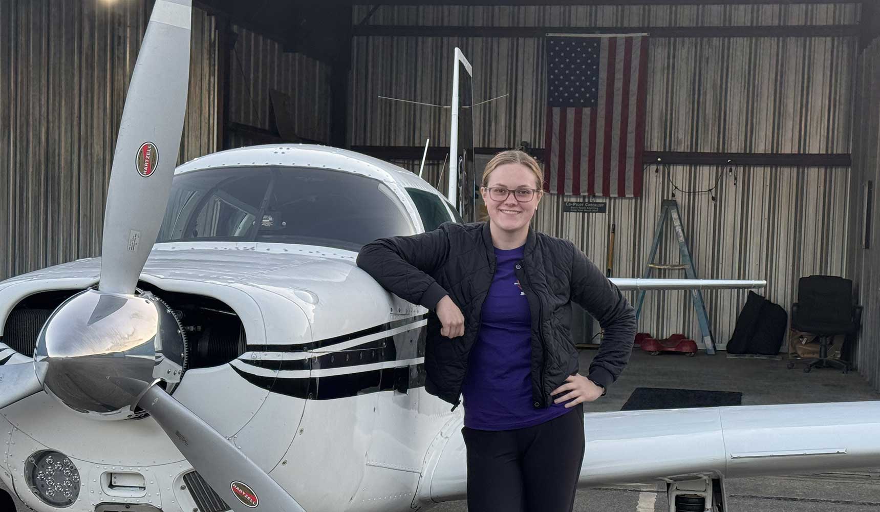 MGA student Annabelle Kellogg stands beside her plane in a hanger.