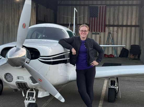 MGA student Annabelle Kellogg stands beside her plane in a hanger.
