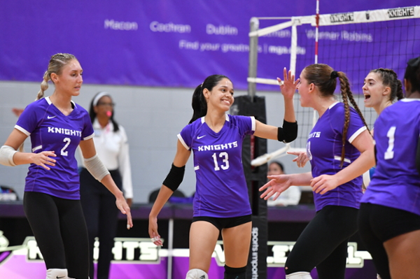 MGA Knights volleyball players celebrate on the court during a game.