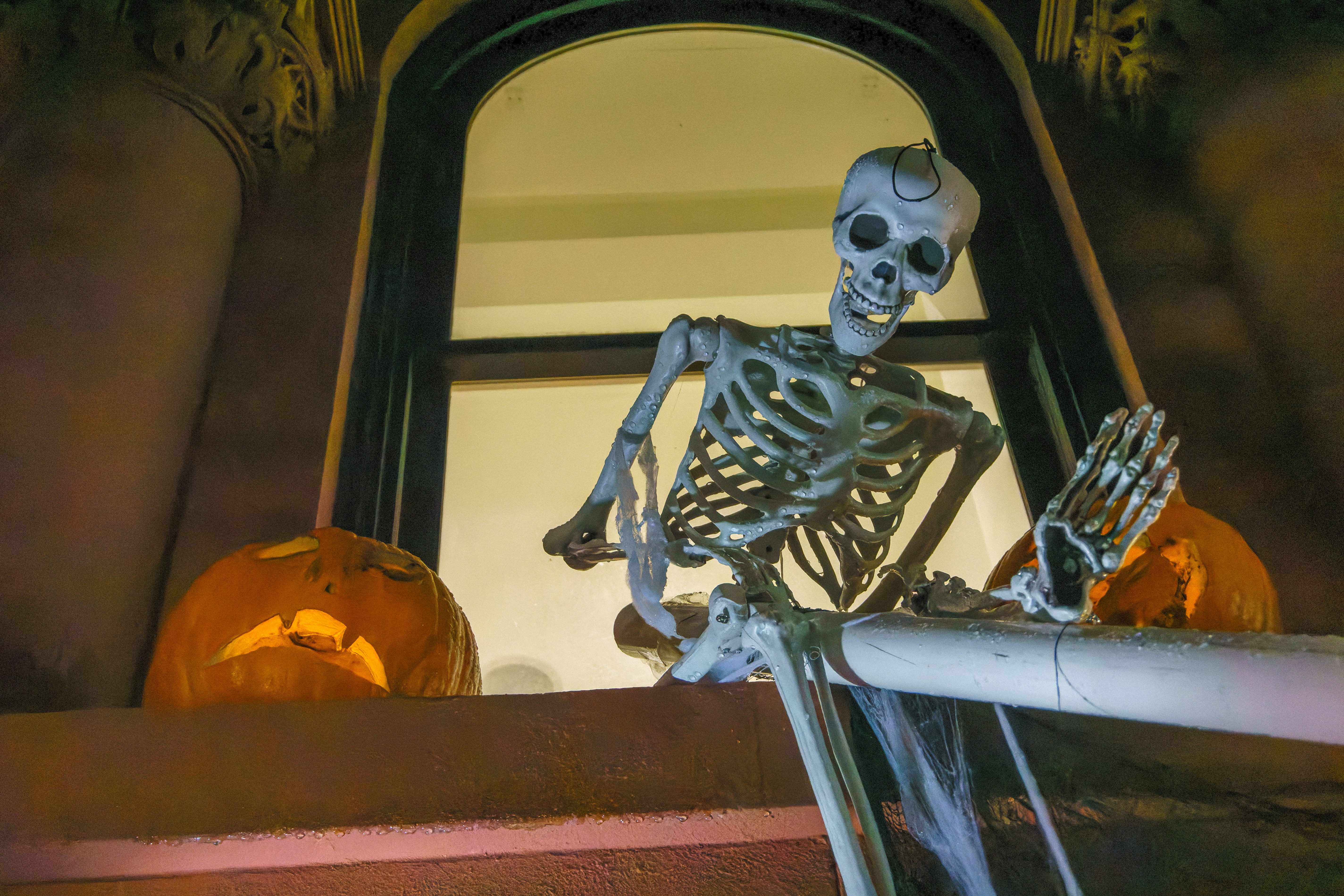 Skeleton and pumpkins sit on a stoop.