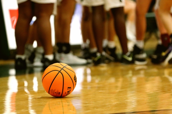 Basketball sits on a court with players huddled behind it.