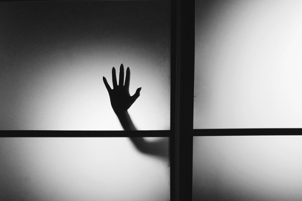 Black and white photo of a silhouette of a hand against glass. 