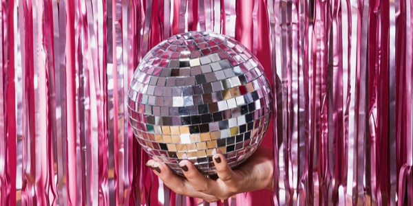 Hand breaking through a pink tinsel wall holding a disco ball.